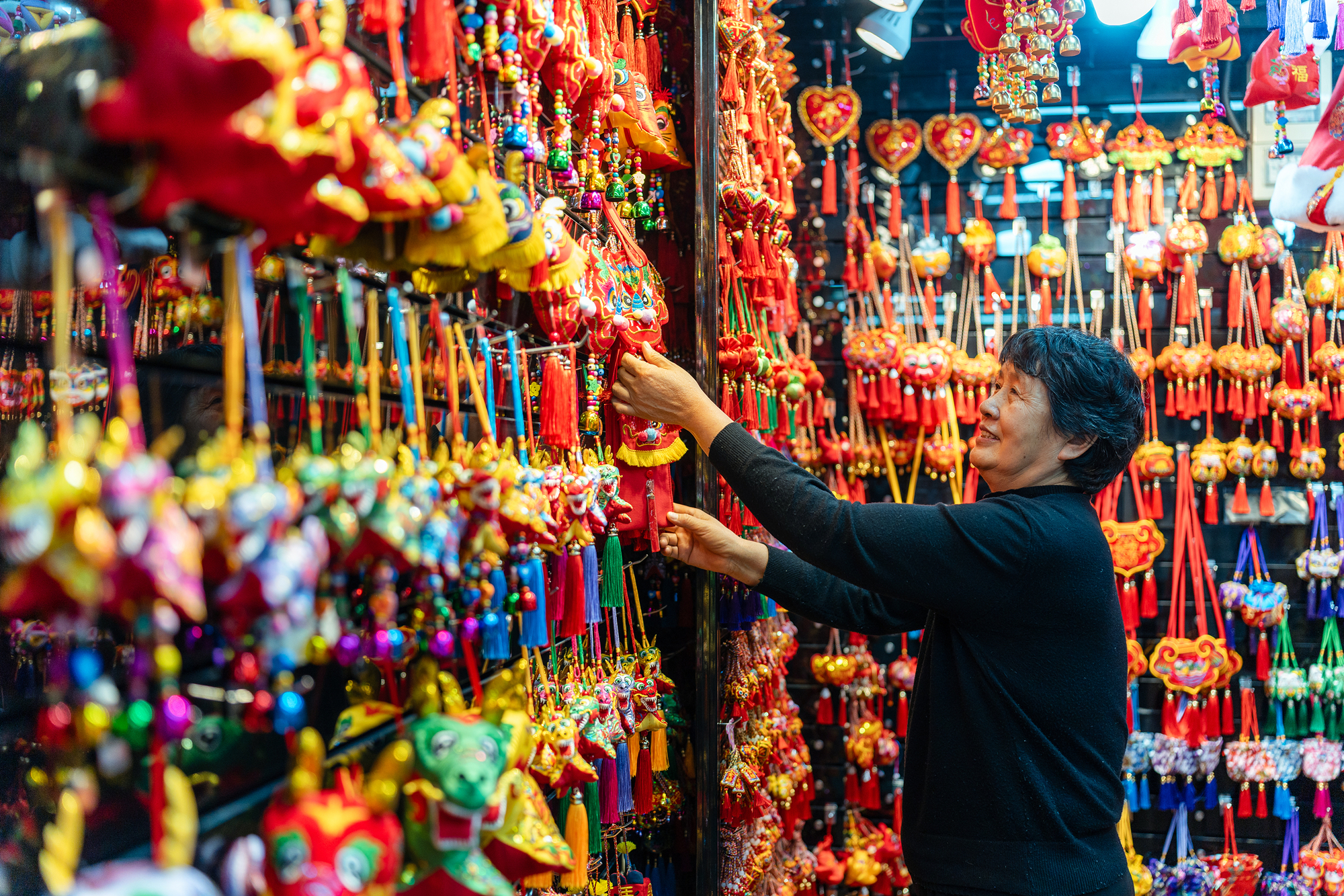 2023年12月11日，金華義烏國(guó)際商貿(mào)城，龍年喜慶用品掛滿攤位，顧客正在挑選中。